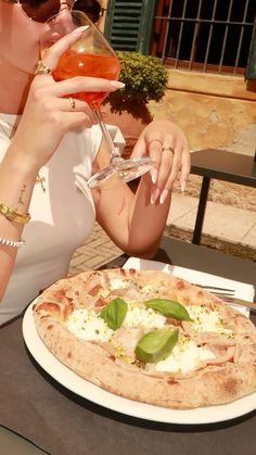 a woman sitting at a table with a pizza and drink in front of her face