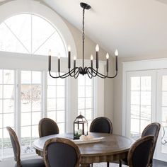 a dining room table with chairs and a chandelier in front of large windows