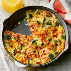 an omelet with broccoli and cheese in a pan next to a glass of orange juice