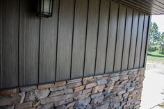 a stone wall next to a building with a lamp on the side and trees in the background