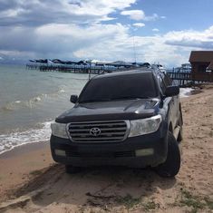 a black suv parked on the beach next to the ocean and pier in the background