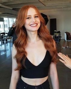 a woman with long red hair smiling and posing for the camera in an office building