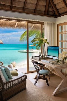 a desk with two computers on it in front of a window overlooking the water and beach