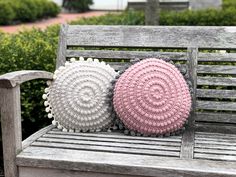 two crocheted pillows sitting on top of a wooden bench