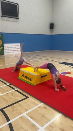 two people doing handstands on top of a yellow box in an indoor gym