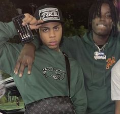 three young men sitting next to each other in front of a car wearing green sweatshirts and hats