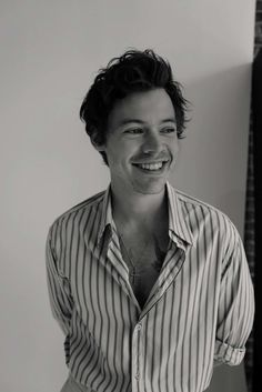 black and white photograph of a smiling man wearing a striped shirt with his hands in his pockets