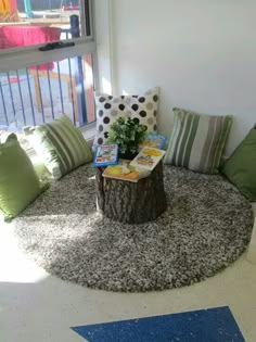 a living room filled with lots of pillows and a tree stump on the floor next to a window