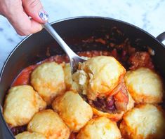 a person holding a spoon in a pot filled with food that includes tater tots