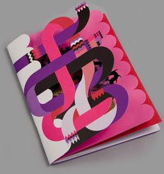 an open book with pink, purple and red designs on the front cover sitting on top of a gray surface