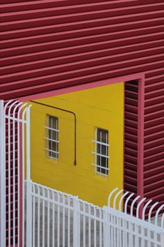 a red and yellow building is seen through a white fence