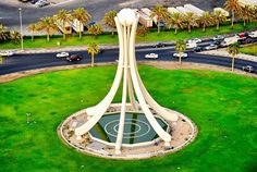 an aerial view of a large clock tower in the middle of a green field with palm trees