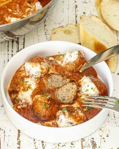 a white bowl filled with meatballs and sauce next to bread on a wooden table