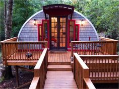 a wooden deck leading up to a tiny cabin in the woods with red doors and windows