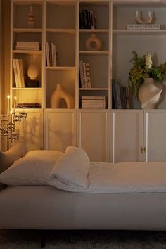 a bed with white sheets and pillows in front of a book shelf filled with books