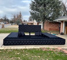 a large black couch sitting on top of a sidewalk next to a green tree and brick building