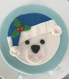 a cake decorated like a polar bear wearing a knitted hat and holly berry decoration