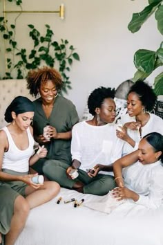 four women are sitting on a bed and one is looking at something in her hand