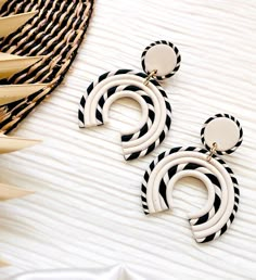 two pairs of black and white earrings sitting on top of a table next to a straw hat