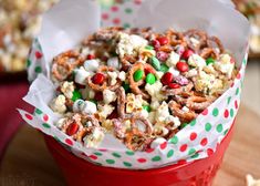 a red bucket filled with cereal and candy mix on top of a wooden table next to other food items