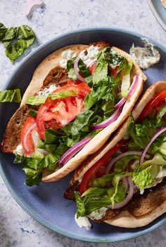 two tacos with lettuce, tomatoes and onions on them sitting on a blue plate