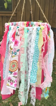 a bunch of different colored ribbons hanging from a string in the grass near a fence