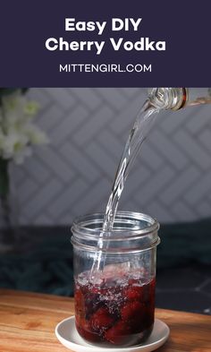 a person pouring water into a glass jar filled with berry soda on top of a wooden table