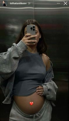 a pregnant woman taking a selfie in front of a mirror with her cell phone