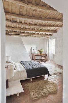 a bed sitting under a wooden ceiling next to a table and chair in a room