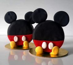 two mickey mouse cakes are sitting on gold plates with black and red ears, one has yellow eyes