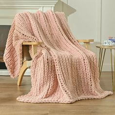 a pink knitted blanket sitting on top of a wooden chair next to a fire place