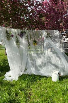 a white sheet draped over a trash can in the grass with flowers hanging from it