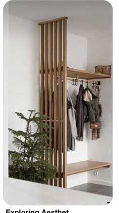 a coat rack with clothes hanging on it next to a potted plant in front of a white wall