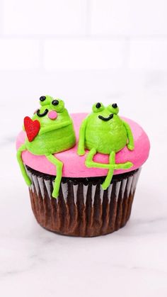 two green frogs sitting on top of a pink cupcake