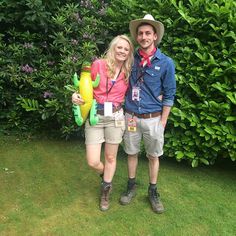 a man and woman are standing in front of some bushes holding fake flowers on the grass