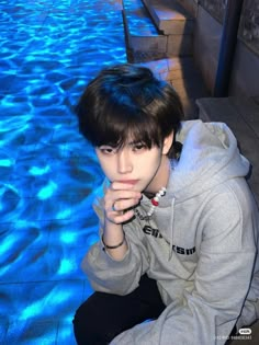 a young man sitting on the edge of a swimming pool with his hands under his chin