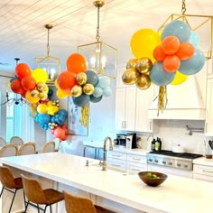 balloons are hanging from the ceiling in a kitchen with white counter tops and chairs around it