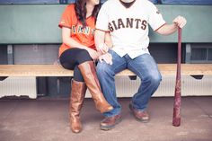 a man and woman sitting on a bench in front of a baseball dugout with a bat