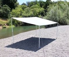 a white tent sitting on top of a sandy beach next to a river with trees in the background