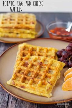 two plates with waffles, orange slices and grapes on them next to some fruit