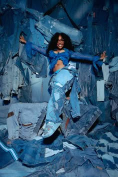 a woman is posing with her arms spread out in front of piles of jean jackets