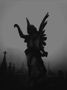 an angel statue standing in the middle of a cemetery on a foggy day with tombstones