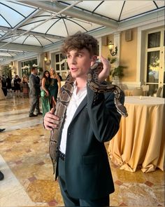 a man in a suit holding a snake up to his ear while standing on a marble floor