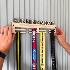 two hands holding up a rack with medals hanging from it's sides in front of a metal wall