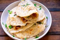 a white bowl filled with pita bread on top of a wooden table