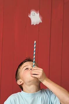 a young boy drinking from a straw in front of a red wall