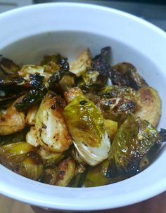 a white bowl filled with cooked brussel sprouts and other food items