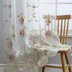 a chair sitting in front of a window covered with sheer curtains and pink flowers on it