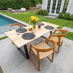 a wooden table with chairs around it in front of a swimming pool and lawn area