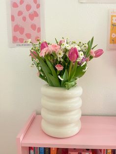 a white vase filled with pink and white flowers on top of a pink book shelf